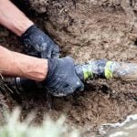 Plumber Repairing a Broken Pipe in a Septic Field